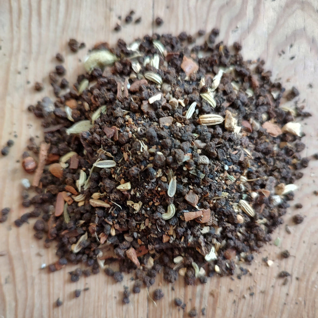 A pile of coarse ground spice blend with visible seeds and small pieces, photographed on a light wood surface.