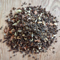A pile of coarse ground spice blend with visible seeds and small pieces, photographed on a light wood surface.