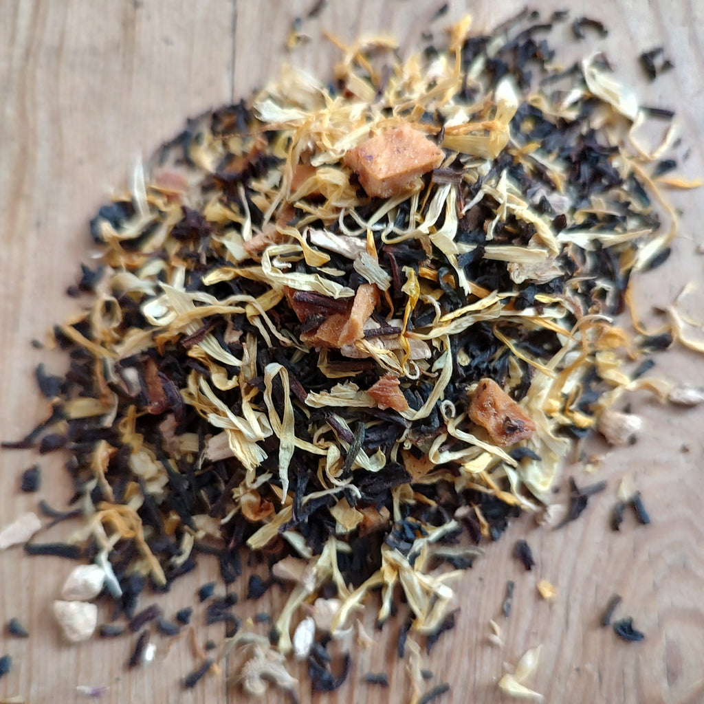 A pile of loose-leaf herbal tea blend containing dried leaves, buds, and small brown pieces, displayed on a light wooden surface.