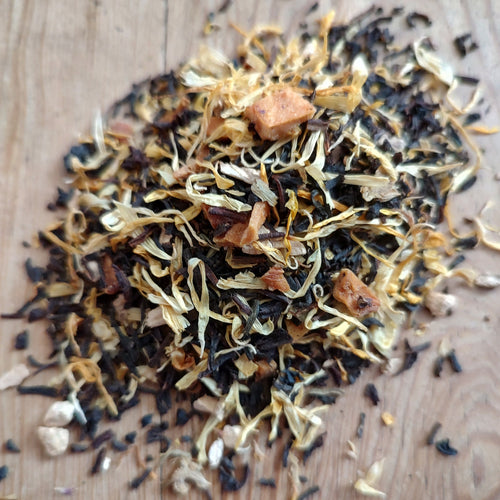 A pile of loose-leaf herbal tea blend containing dried leaves, buds, and small brown pieces, displayed on a light wooden surface.