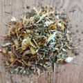 A small pile of loose dried herbal tea blend on a light brown wooden surface.